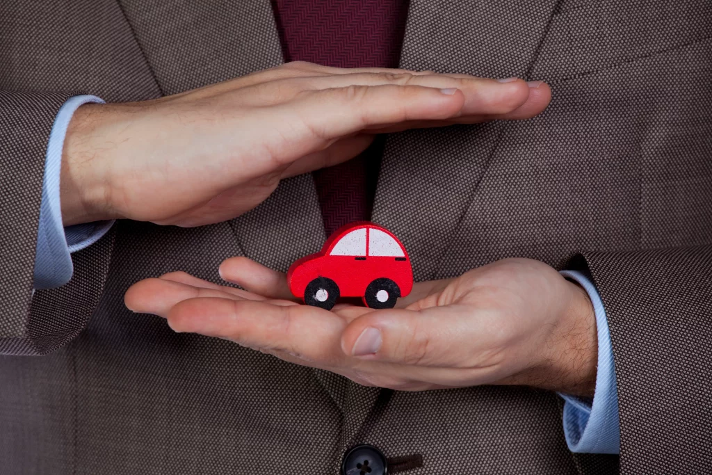 hands covering toy car to depict auto insurance